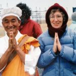 A woman and man smiling together for a picture outdoors while having their hands in a praying position.
