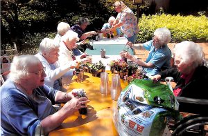 Nine people sitting outdoors at a long table working together planting small plants.