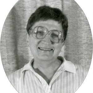 A black and white head shot of a woman with short dark hair, big glasses, and a striped collared shirt.