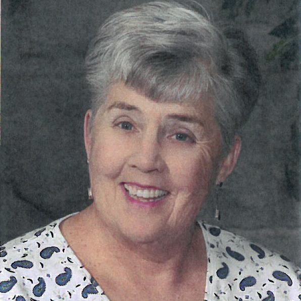 A portrait headshot picture of a woman with short grey hair wearing patterned scrubs smiling brightly.