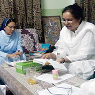 Four religious women sit in a living room while one is reading from a book while the others listen.
