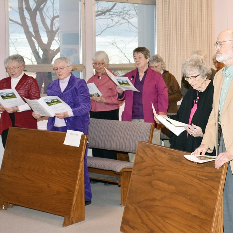 A church service with attendees standing and singing together while reading booklets.