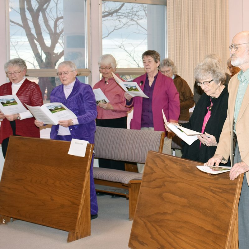 A church service with attendees standing and singing together while reading booklets.