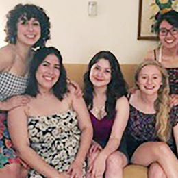 5 women sitting together on a couch in a living room for a group picture.