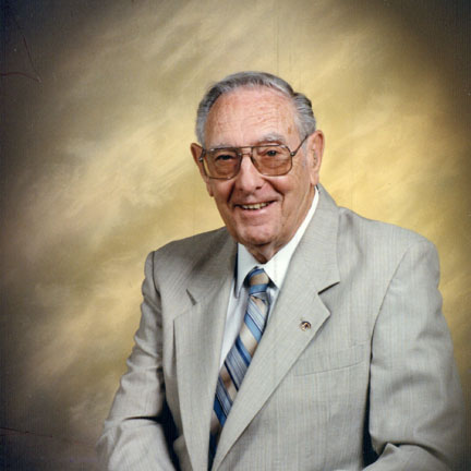 A man wearing glasses and a grey suit with a striped tie smiling for a portrait picture.