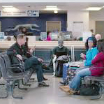 A Greyhound bus station waiting room with numerous people sitting and waiting for their bus.