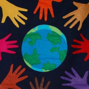 A graphic symbolizing community and connection. A blue and green world graphic with different colored hands surrounding it on a black background.
