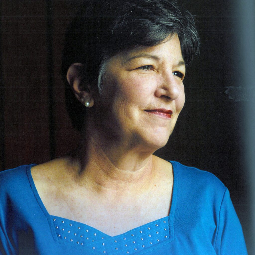A woman with short brown hair wearing a blue blouse smiling candidly looking off to the side for a portrait headshot picture with a plain black background.