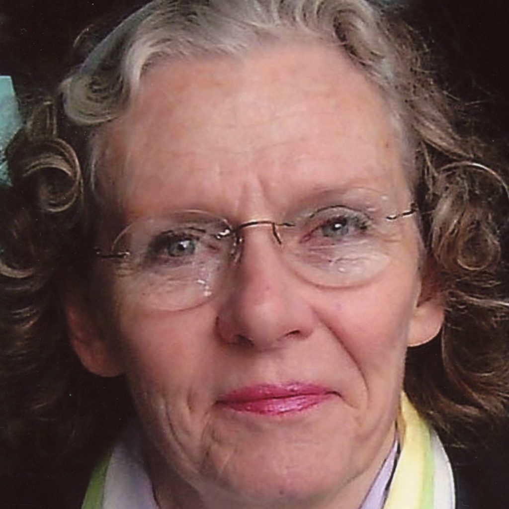A head shot of a woman smiling with short curly hair, wearing glasses, and a colored scarf.
