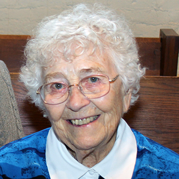 A woman with short white hair smiling brightly for a headshot picture indoors.