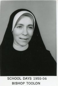 A black and white portrait picture of a nun smiling for a with a grey plain background.