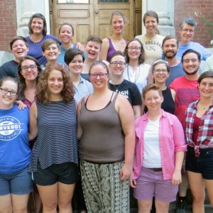 A group photo of many people smiling brightly while standing on the front steps of a red brick building.