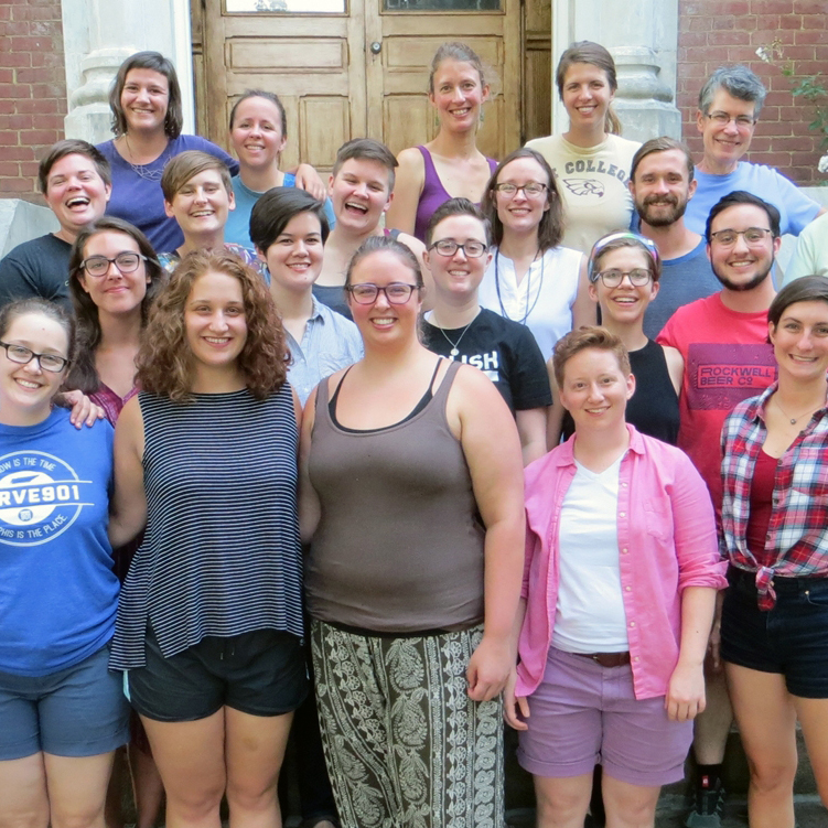 A group photo of many people smiling brightly while standing on the front steps of a red brick building.
