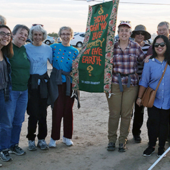 12 women attending an outdoor protest with one banner displayed in between them.