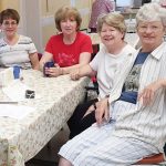 7 women smiling together for a group picture while sitting at a dining table indoors.