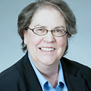 A woman with short brown hair and oval-shaped glasses smiling brightly for a headshot picture in business attire.