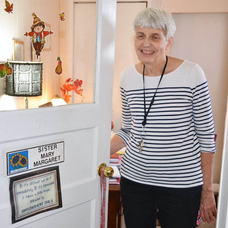 A woman with short grey hair standing in a white doorway smiling for a picture indoors.