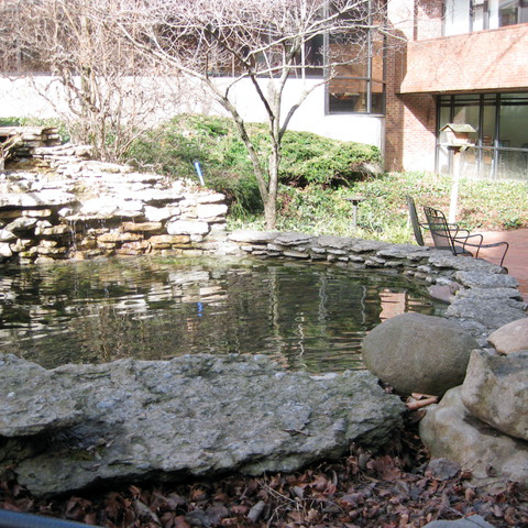 A courtyard with a pond, and a red brick path in front of a red and white brick building.