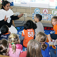 A woman teaching children sitting on the floor in a classroom.