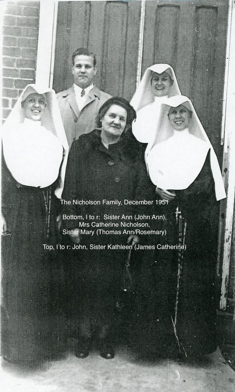 A black and white picture of three nuns, one woman in a black blazer and skirt, and one man standing together on the front steps of a building smiling together for a picture.