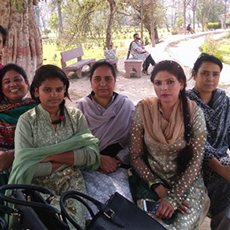 Six women sitting together and smiling for a picture outdoors in a park.