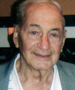 A man with short grey hair, smiling brightly for a headshot picture indoors, wearing a white shirt, with a grey blazer.