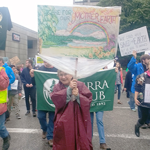A woman with a large sign smiling at a protest for saving the Earth on a rainy day.