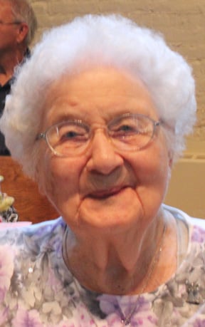 A woman with white short hair and glasses smiles for a picture indoors.