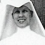 A black and white headshot of a nun brightly smiling for a picture.