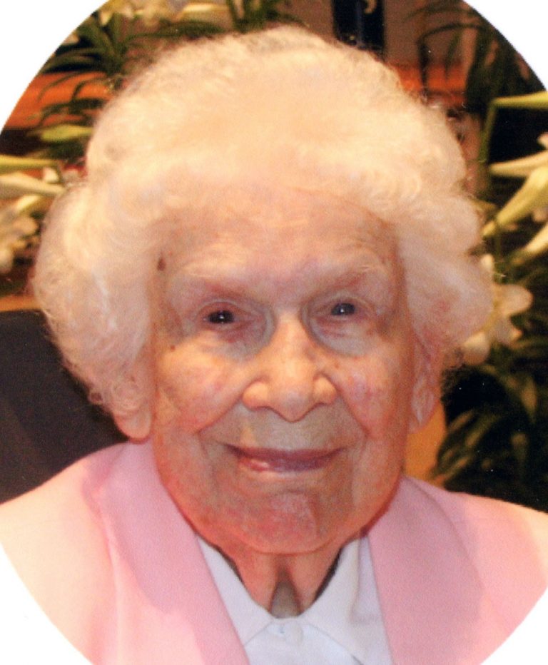 A woman with short white hair smiling for a headshot picture wearing a white shirt and a light pink cardigan.