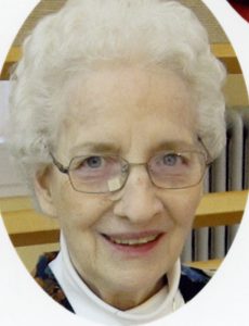 A woman with short white hair, and glasses smiling for a headshot picture in a white turtleneck and a dark colored cardigan.