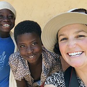 A woman and two young kids smiling together for a selfie outdoors on a building patio on a sunny day.