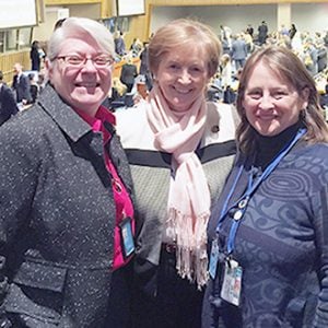 Three women smiling together for a group picture at a social event indoors.