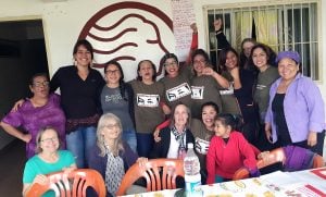 15 women smiling together for a group picture indoors.