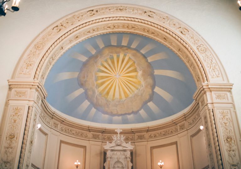 An intricate archway with a painting of sun rays on a blue background.