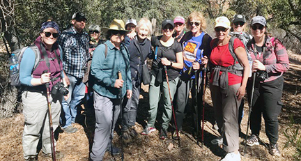 12 hikers stop and smile for a group picture mid-trail on a sunny day.