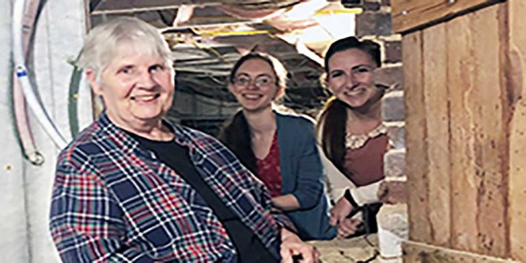 Three women smiling for a picture while exploring a basement crawl space.