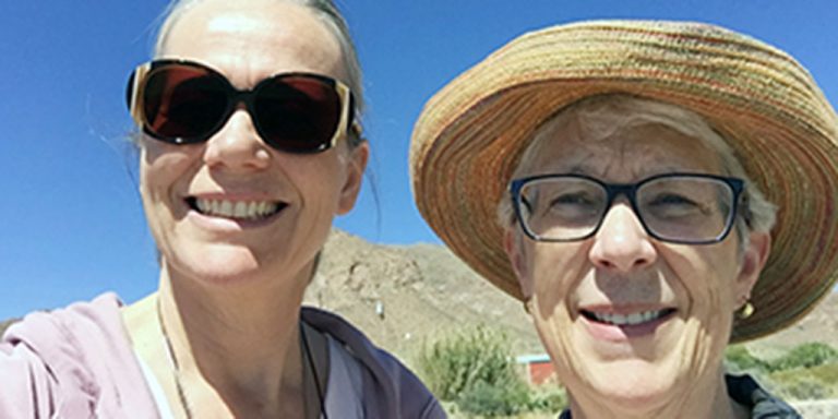 Two women smiling for a selfie picture outdoors on a sunny day.