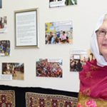 A woman wearing Pakistani attire smiling brightly in a classroom next to a collage wall of Pakistani appreciation.