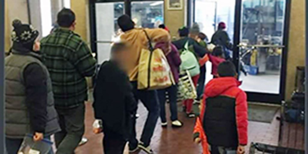 Passengers dressed in warm winter gear leave the building through glass doors.