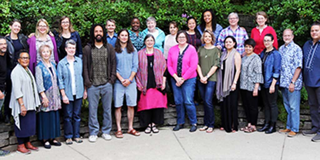 A large group photo of diverse individuals standing outdoors in front of large green trees.