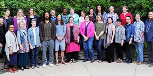A large group photo of diverse individuals standing outdoors in front of large green trees.