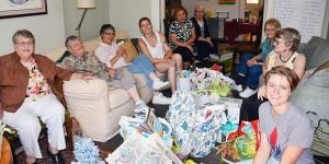 Nine women sitting together in a living room with assorted donations. They are sorting, and planning for donations to be given to those in need.