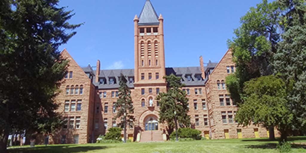 A large red brick building with a large tower in the center and big green trees on either side.
