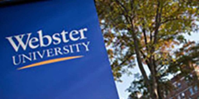A royal blue with white lettering sign for Webster University with a background of large leafy trees.