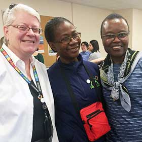 Three women smiling together for a group picture at an indoor social event.