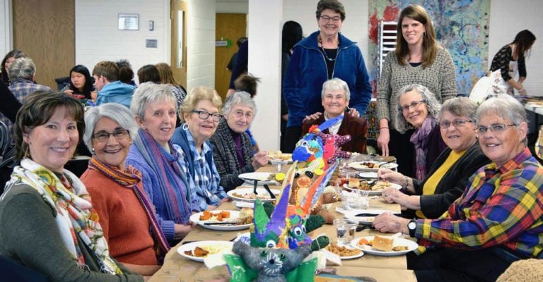 A group of women of varying ages sit smiling around a banquet table.