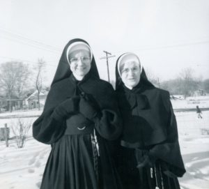 Photo of two sisters standing out in the snow in winter habits