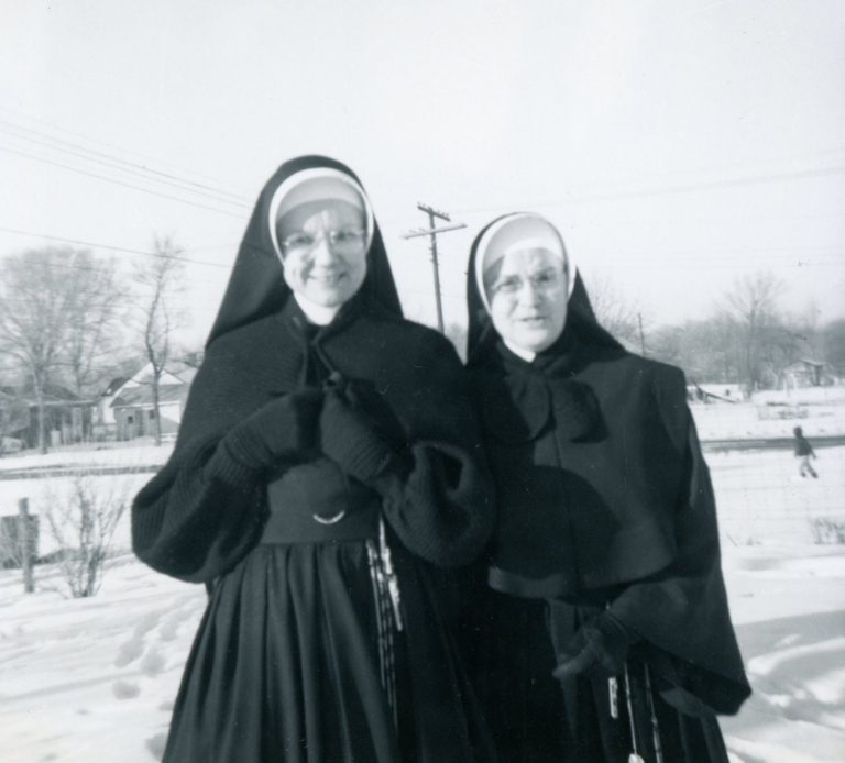 Photo of two sisters standing out in the snow in winter habits