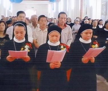 A religious vow ceremony crowd standing inside a church. Mostly nuns, with some men wearing white button-up shirts they're all reading white paper booklets.